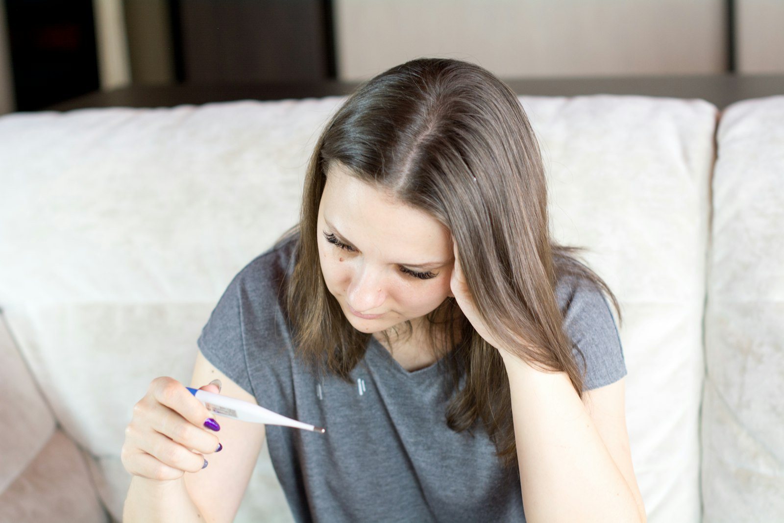 A person sitting on a bed holding a thermometer